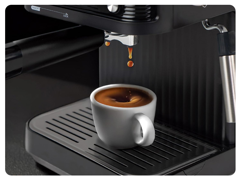 Primo piano della macchina per caffè espresso che eroga caffè scuro in una tazza di ceramica bianca su vaschetta raccogligocce nera con superficie increspata.