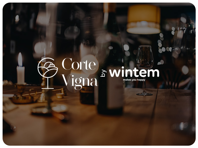 Tavolo poco illuminato con bicchieri da vino, bottiglie e candele. Il testo sovrapposto recita ?Corte Vigna by wintem? con il logo stilizzato di un bicchiere di vino.