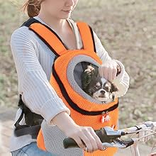 Zaino porta animali arancione con finestra a cupola trasparente. Persona che lo indossa mentre va in bicicletta, cane di piccola taglia visibile all'interno.