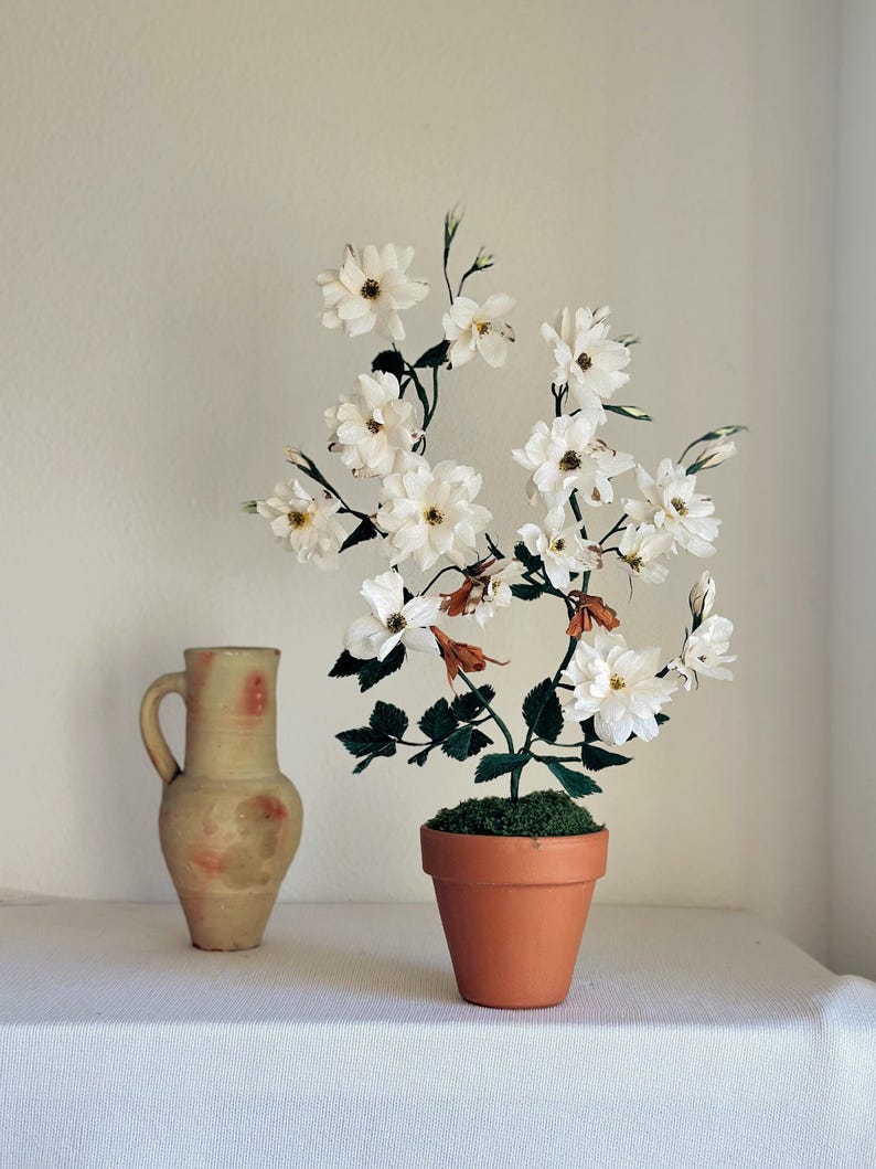Rosa blanca realista hecha de papel crepé en una maceta de terracota.