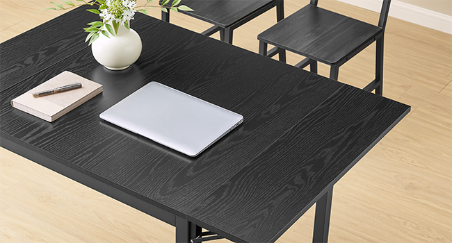 Scrivania moderna con struttura in legno nero con computer portatile e vaso bianco, accompagnata da sedie nere abbinate su