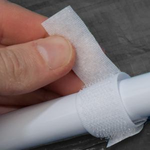 Primo piano di un dito che applica del nastro medicale bianco su un oggetto cilindrico, dimostrando le proprietà adesive e la flessibilità
