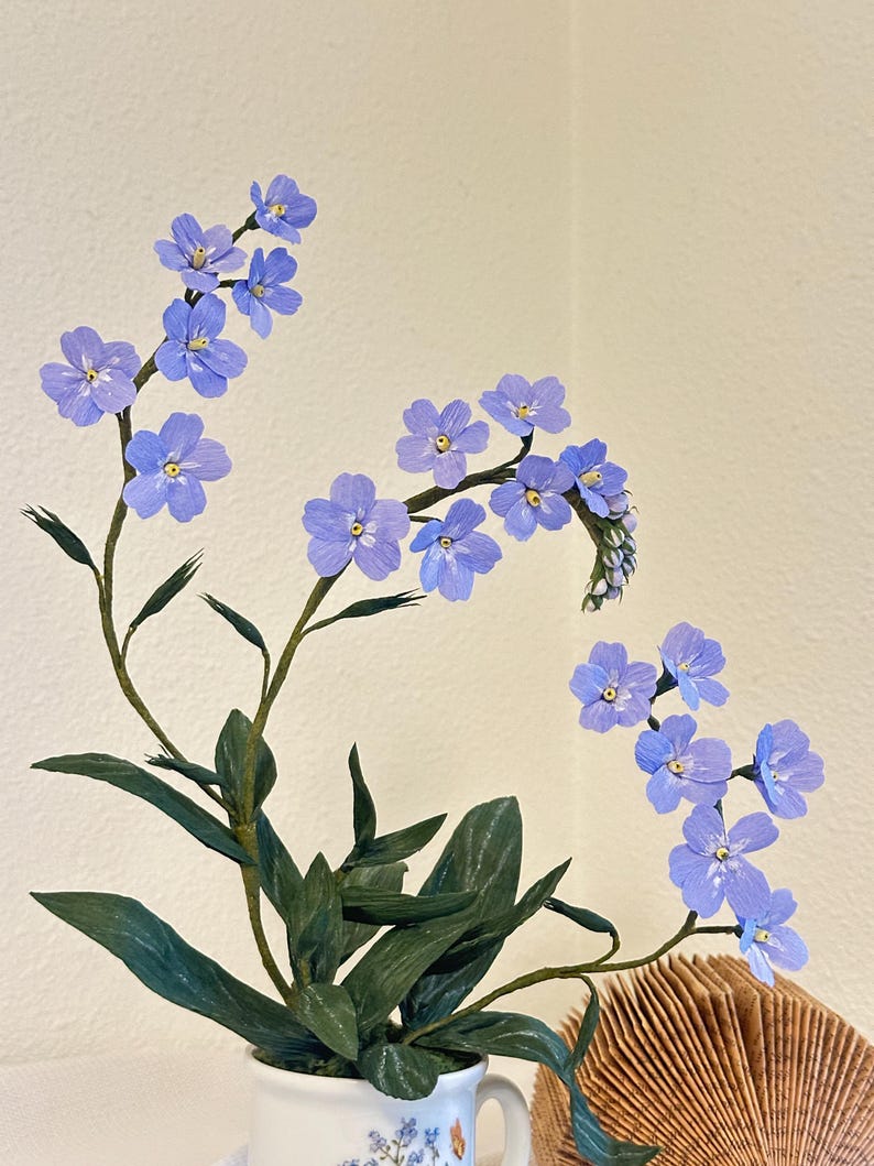 Nomeolvides azules hechos de papel crepé en una taza de té.