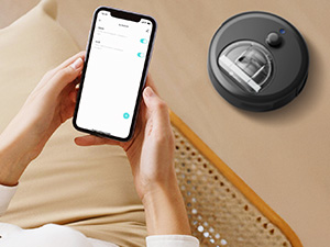 Persona che tiene in mano uno smartphone con interfaccia app visibile, accanto a un aspirapolvere robotico circolare con scomparto per la polvere visibile su una superficie beige