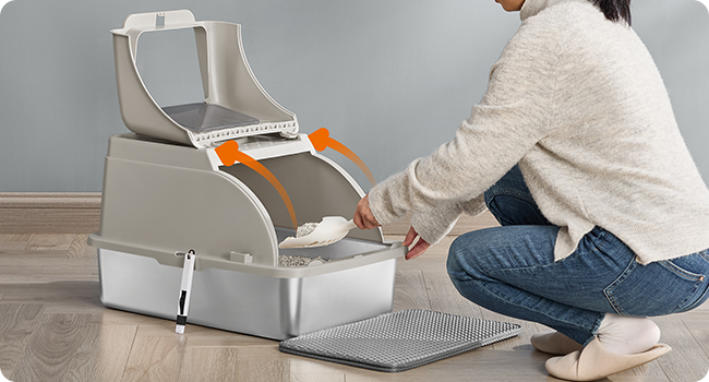Mangiatoia automatica per animali domestici con doppio scomparto. Una persona dimostra di aprire il coperchio superiore, rivelando l'area di conservazione degli alimenti. Tappeto grigio visibile in primo piano