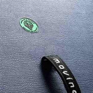 Dettaglio ravvicinato di un braccialetto o braccialetto nero su uno sfondo tessile grigio, con piccolo elemento decorativo verde visibile.