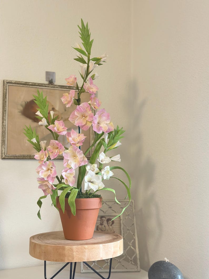 Flores de gladiolos hechas de papel crepé realista en una maceta de terracota.