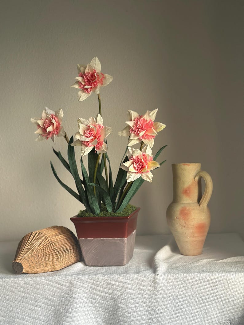 Dos flores de narciso realistas de papel crepé en una maceta de cerámica.