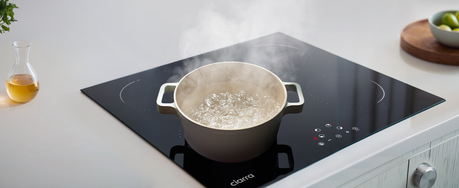 Piano cottura a induzione con pentola in acciaio inossidabile che fa bollire l'acqua. Elegante superficie nera con comandi touch, posizionata in un piano di lavoro della cucina accanto al